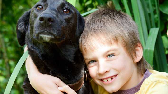 Ein Junge umarmt einen großen, schwarzen Hund (Quelle: Colourbox)