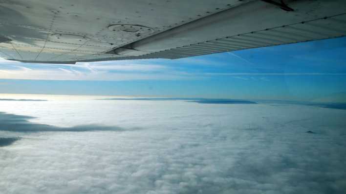 Blick aus einem Flugzeug, oben die Tragfläche, darunter ein dichter, weißer Wolkenhimmel (Quelle: imago images/Stefan Noebel-Heise)