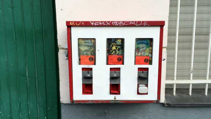 Kaugummiautomat an einer Häuserwand, links eine grüne Holztür, rechts ein vergittertes Fenster (Quelle: rbb/OHRENBÄR/Birgit Patzelt)