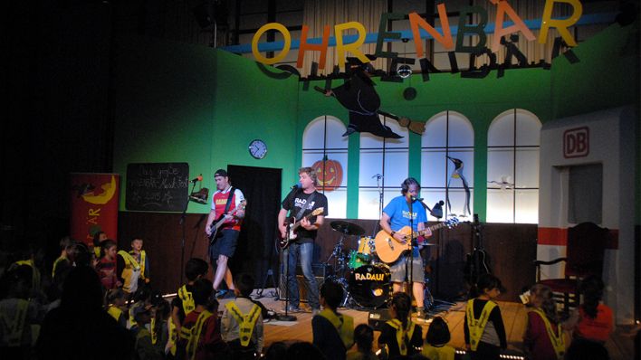 Blick auf die OHRENBÄR-Musik-Fest-Bühne, die Band Radau spielt und Kinder hören gespannt zu (Quelle: rbb/OHRENBÄR/Birgit Patzelt)