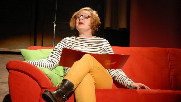 Autorin Karen Matting, auf der roten Couch, mit einer Lesemappe, blickt ins Publikum (Quelle: rbb/OHRENBÄR)