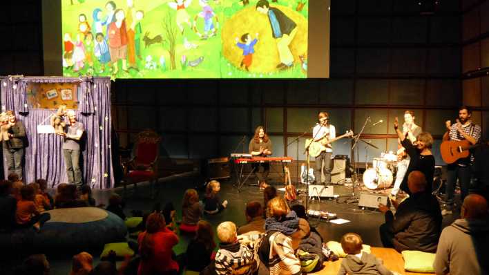 Publikum vor der Bühne mit Band und der WDR-Bärenbude, darüber eine bunte Bildprojektion mit gezeichneten Figuren (Quelle: rbb/OHRENBÄR/Sonja Kessen)