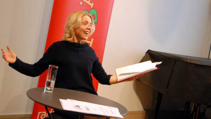 Schauspielerin Antje von der Ahe liest, mit ausgebreiteten Armen, den Text in der rechten Hand (Quelle: rbb/OHRENBÄR/Birgit Patzelt)