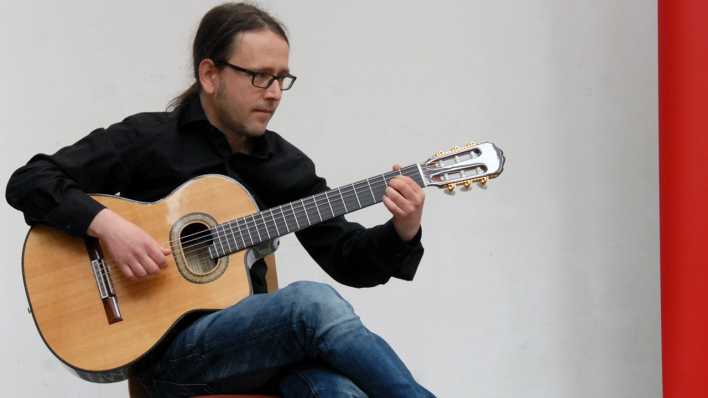 Musiker Jacob Jurgeit spielt Gitarre, sitzt auf einem Stuhl (Quelle: rbb/0HRENBÄR/Birgit Patzelt)