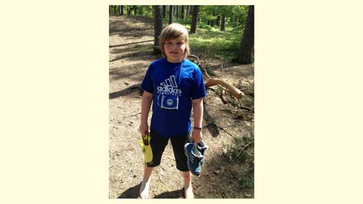 Anton Schanz, einer der Sieger des OHRENBÄR-Schreibwettbewerbs, steht im Wald mit nackten Füßen, die Sportschuhe in der Hand © Privat