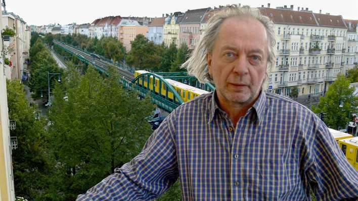 Porträt des Autors Wilfried Bergholz, im Hintergrund eine Häuserfront und eine gelbe U-Bahn (Quelle: N. Weidemann)