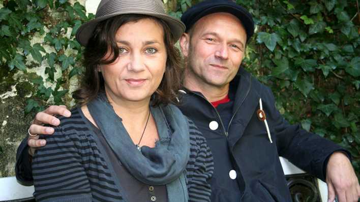 Die Autoren Anja Kömmerling und Thomas Brinx sitzen gemeinsam auf einer Bank (Quelle: privat)