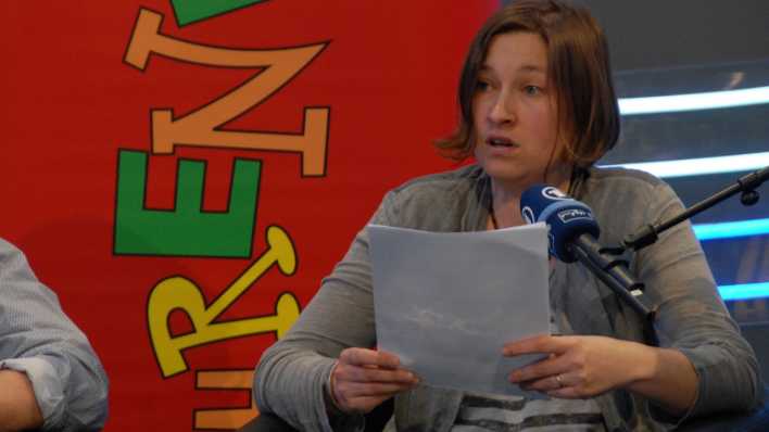 Autorin Ariane Grundies liest, in beiden Händen hält sie das Manuskript, im Hintergrund ein OHRENBÄR-Banner (Quelle: rbb/OHRENBÄR/Birgit Patzelt)