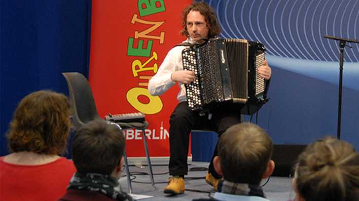 Musiker Uwe Steger spielt das Akkordeon, im Hintergrund ein OHRENBÄR-Banner (Quelle: rbb/OHRENBÄR/Birgit Patzelt)