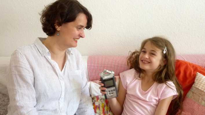 Kinder-Reporterin Hannah gemeinsam mit Illustratorin Daniela Bunge im Interview, auf der Couch, mit einem Aufnahmegerät, sie lachen (Quelle: rbb/OHRENBÄR/Alja Mai)