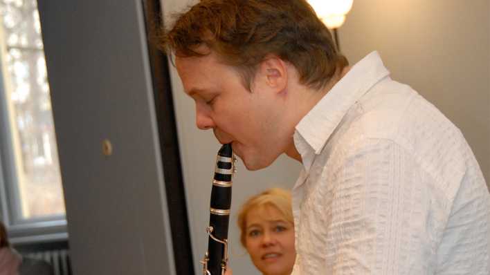 Friedemann Matzeit spielt auf der Klarinette, Schauspielerin Astrid Kohrs im Hintergrund, schaut zu (Quelle: rbb/OHRENBÄR/Birgit Patzelt)