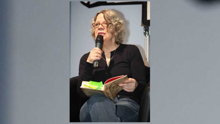Autorin Martina Dierks auf einer Bühne, liest mit Mikrofon und Buch in den Händen (Quelle: imago images/Gerhard Leber)