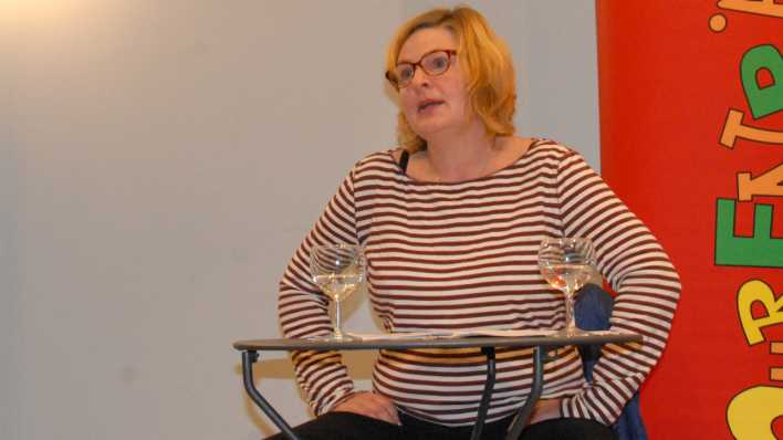 Autorin Karen Matting sitzt am Tisch und erzählt zum Publikum, rechts das rote OHRENBÄR-Banner (Quelle: rbb/OHRENBÄR/Birgit Patzelt)