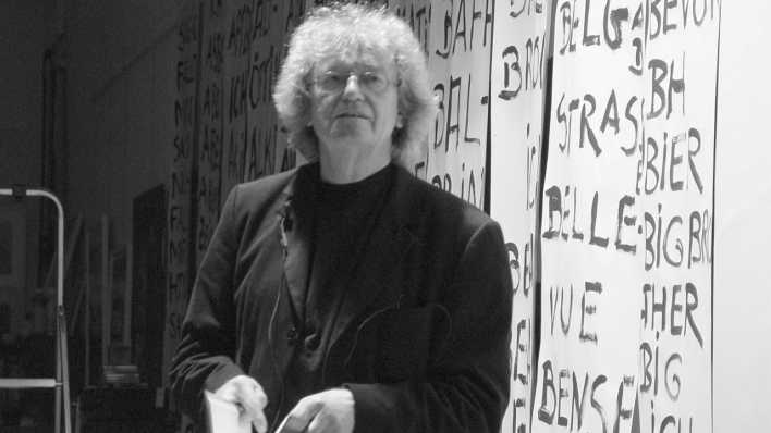 Porträt des Autors Alfred Gulden vor weißen Bahnen mit Schrift an einer Wand (Quelle: Volker Schütz)