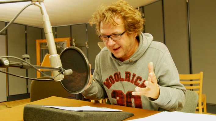 Schauspieler Andreas Fröhlich sitzt am Studiotisch, vor ihm das Mikrofon und das Manuskript © rbb/Redaktion OHRENBÄR