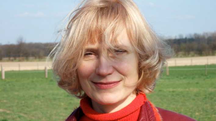 Porträt der Autorin Ulrike Klausmann, auf einer Weidefläche, im Hintergrund Wald (Quelle: privat)