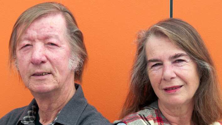 Porträt der Autoren Heidi Knetsch und Stefan Richwien vor einer orangefarbenen Wand (Quelle: privat)