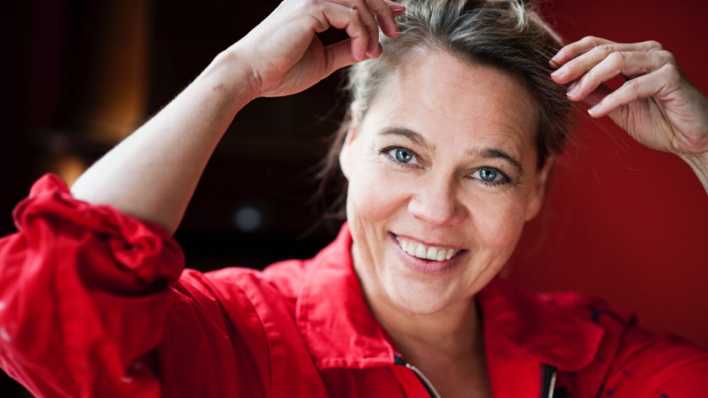 Porträt der Schauspielerin Astrid Kohrs mit roter Jacke, Hände am Kopf (Quelle: Bernd Brundert)