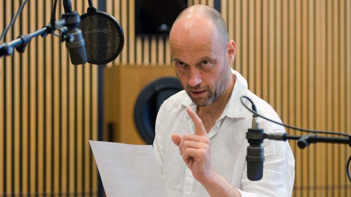 Christian Koerner als Vater vor dem Mikrofon im Studio, im weißen Hemd, linker Zeigefinger erhoben (Quelle: rbb/Oliver Ziebe)