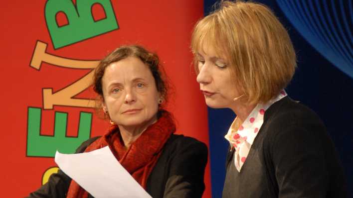 Schauspielerin Nina Petrick liest, Autorin Annette Herzog hört zu, im Hintergrund das rote OHRENBÄR-Banner (Quelle: rbb/OHRENBÄR/Birgit Patzelt)