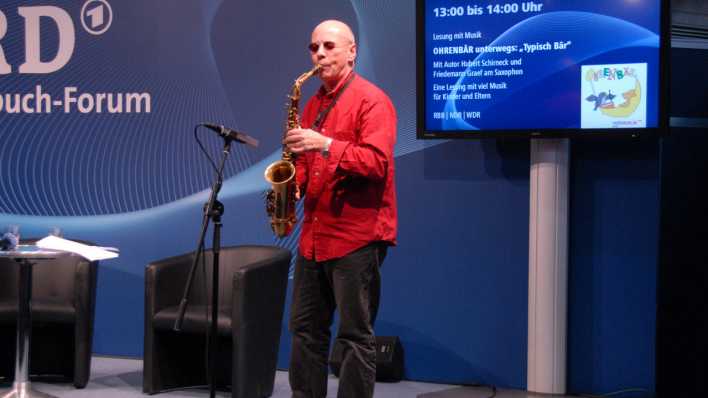 Friedemann Graf spiel auf der Bühne Saxophon. Im Hintzergrund ein Bildschirm mit dem OHRENBÄR-Messeprogramm. © rbb/Redaktion OHRENBÄR