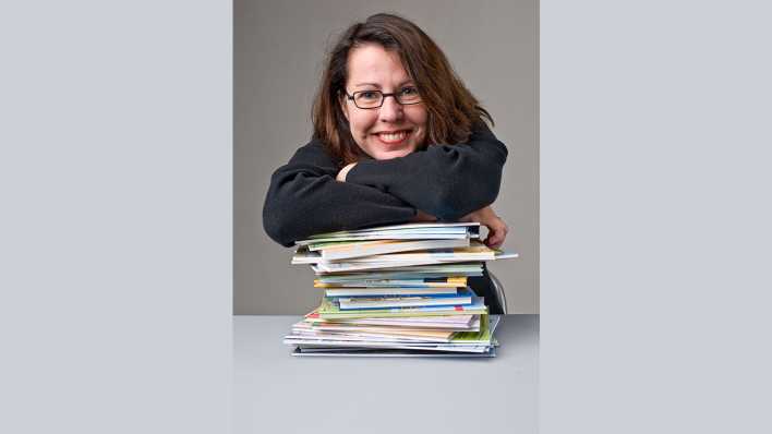 Porträt der Autorin Annette Neubauer, stützt sich freudig auf einen Stapel Bücher (Quelle: privat)