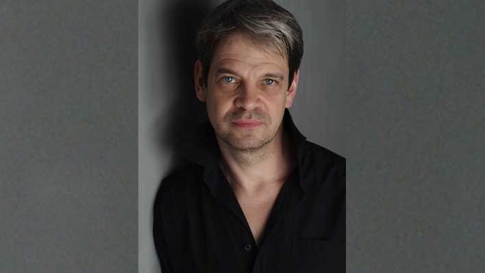 Porträt des Schauspielers Uwe Neumann, an einer Wand gelehnt, mit Schatten (Quelle: Anette Daugardt)