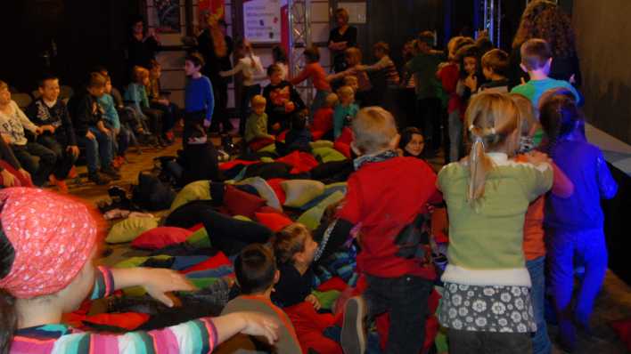 Viele Kinder, die in Schlangenform durch den kleinen Sendesaal laufen, in der Mitte viele bunte Kissen (Quelle: rbb/OHRENBÄR)