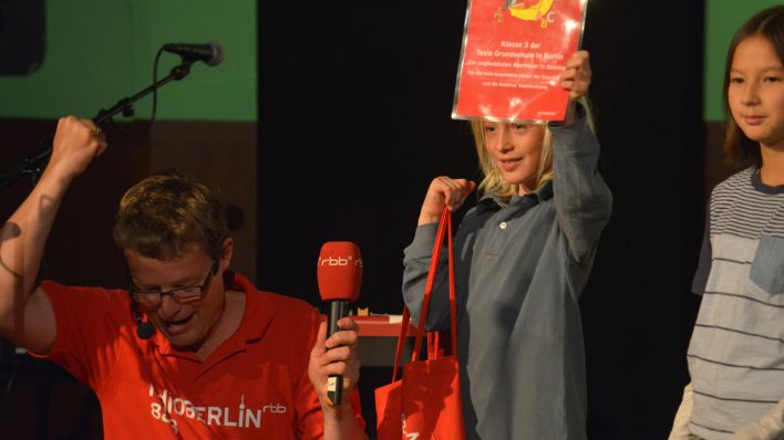 Moderator Alexander Schurig kniet vor den Gewinnern des Sonderpreises, mit Jurikind Yukino (Quelle: rbb/Thomas Ernst)
