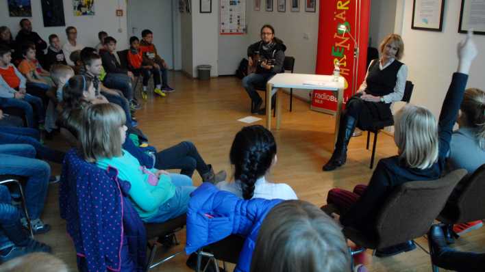 Kinder und Erwachsene lauschen der Lesung von Nina Petrick und dem Spiel von Gitarrist Jacob Jurgeit (Qoelle: rbb/OHRENBÄR/Birgit Patzelt)