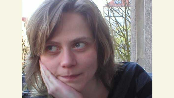 Porträt der Autorin Katharina Schlender, vor einem Fenster, eine Hand am Kinn (Quelle: privat)