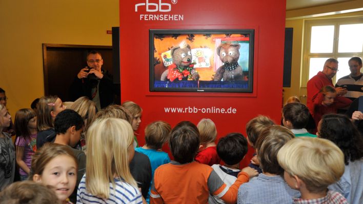 Viele Kinder schauen auf einen großen Bildschirm, auf dem die Bären "Johannes und Stachel" aus der Bärenbude vom WDR 5 zu sehen sind © Thomas Ernst