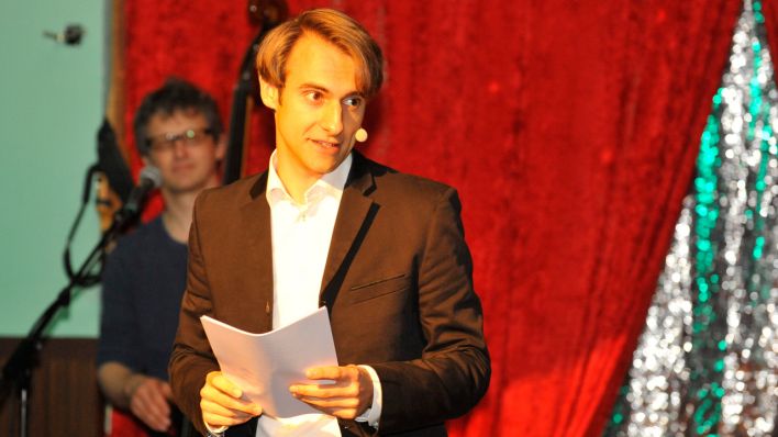 Moderator Marc Langebeck hält Zettel in der Hand und spricht ins Headset © Thomas Ernst