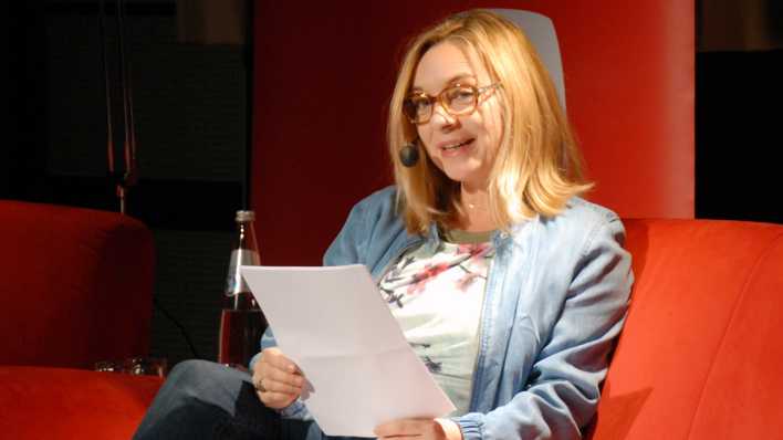 OHRENBÄR-Autorin Jeanette Wagner auf der roten Couch, sie liest eine Geschichte vor (Quelle: rbb/OHRENBÄR/Birgit Patzelt)