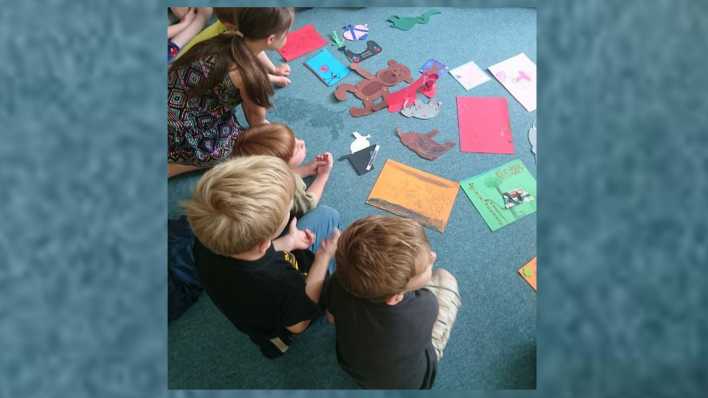 Kinder sitzen auf einem blauen Boden und schauen sich Zeichnungen und Basteleien an (Quelle: rbb/OHRENBÄR/Melanie Himmer)