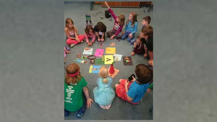 Kinder sitzen in einer Runde auf einem grauen Boden, in der Mitte sind Zeichnungen und Basteleien (Quelle: rbb/OHRENBÄR/Melanie Himmer)