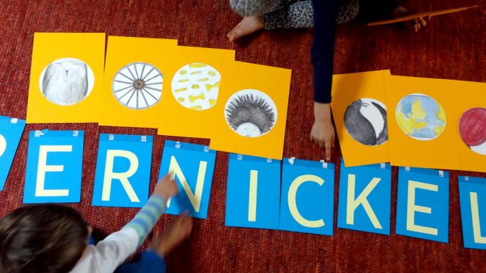 Kinder legen Buchstabenkarten zu den Detailkarten, zu lesen ist: "Pumpernickel" (Quelle: rbb/OHRENBÄR/Martha Zan)
