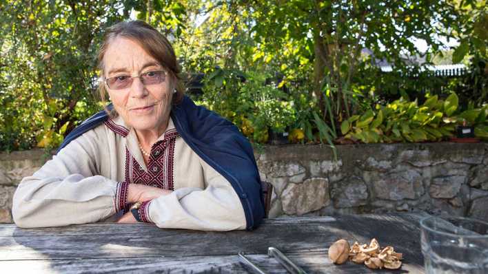 Porträt der Autorin Renate Welsh, sitzt an einem Tisch im Freien, im Hintergund Bäume (Quelle: Markus Roessle)